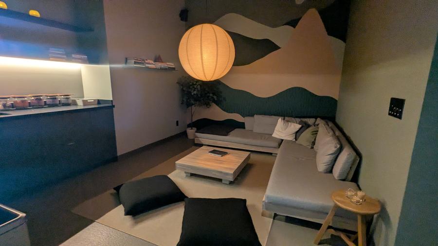 Alter Toronto sauna dry lounge at the Leslieville location — mountain mural, L-shaped sectional couch, globe pendant lantern, and complimentary tea bar