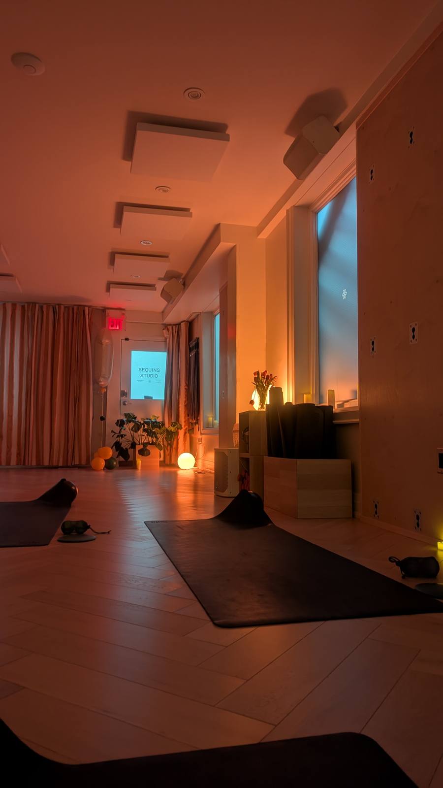 Sequins Studio interior — warm amber lighting, yoga mats laid out, glowing orb lamps, Sequins Studio screen