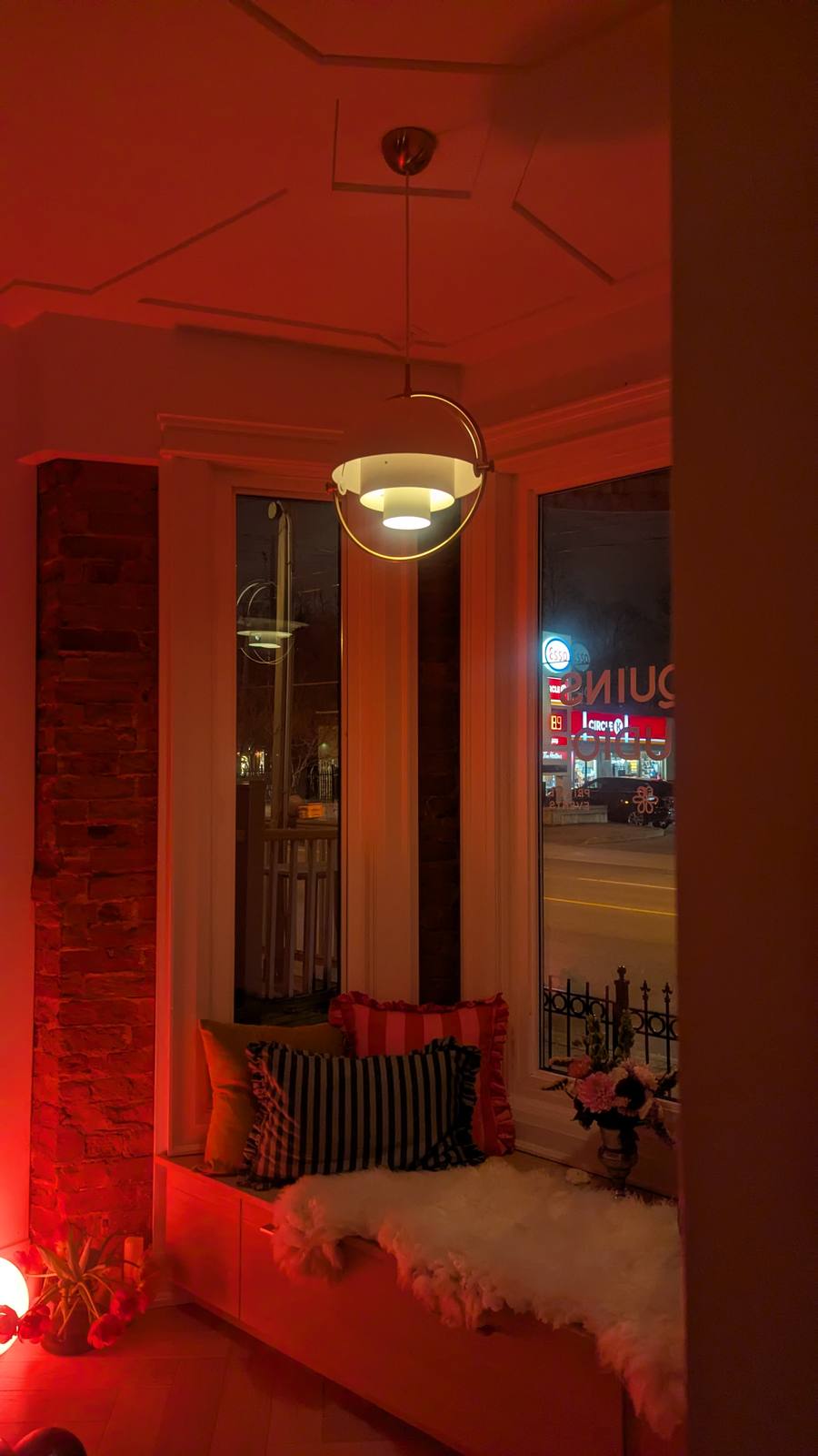 Sequins Studio bay window nook — striped cushions, pendant light, exposed brick, warm red-toned lighting